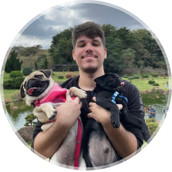 Foto de Raphael Tardin segurando seus dois cachorros da raça pug no colo e um lago com árvores ao fundo